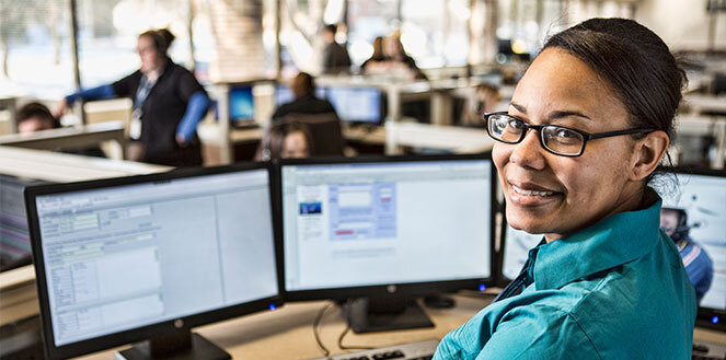 Woman smiling in front of computer monitors.