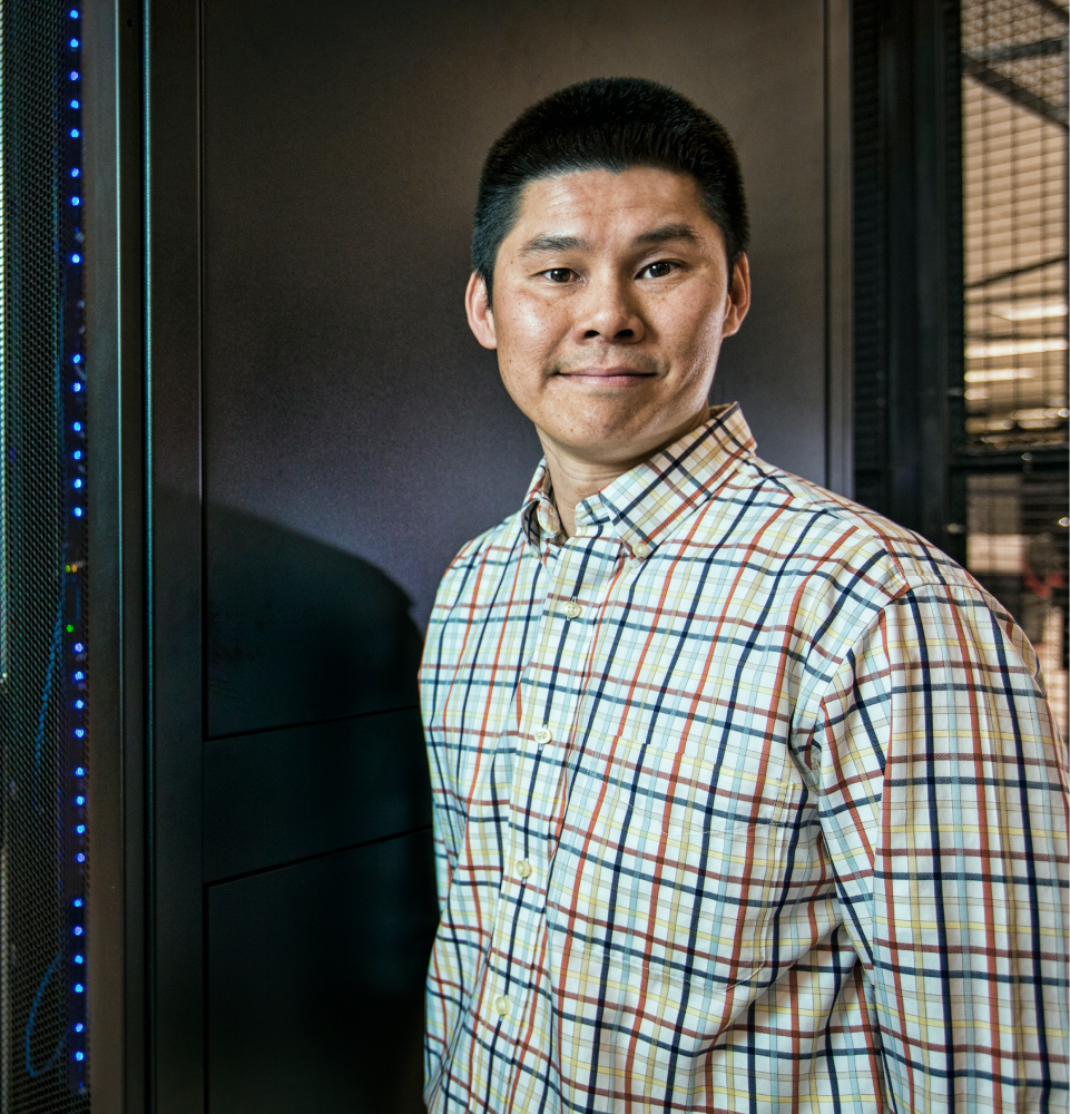 Man standing against computer servers smiling at camera.