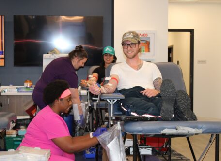 Nurse kneels near man donating blood.