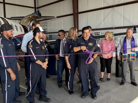 Native Air crew stands as a group behind a purple ribbon while one crew member prepares to cut it with giant scissors
